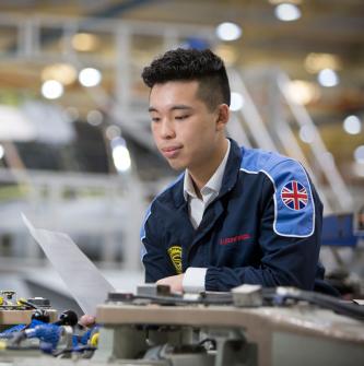 Young East Asian man looks at document while working at Leonardo helicopter facility in Yeovil