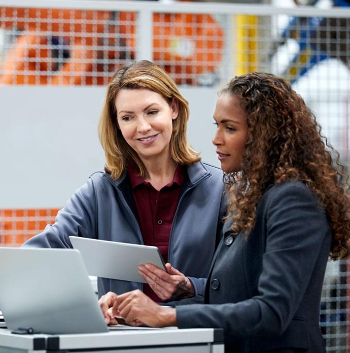 Two women of mixed ethnicity smile as they look at laptop together