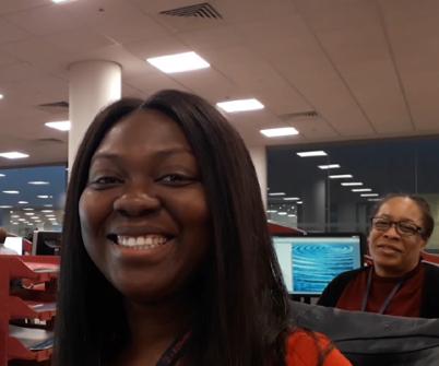 2 ladies smile to camera, sitting at desks