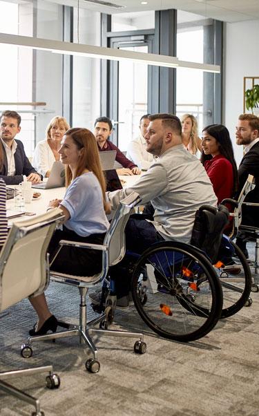 A diverse group of colleagues in a meeting, with one person sitting in a wheelchair