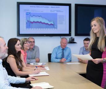 Young woman presents to older colleagues in boardroom