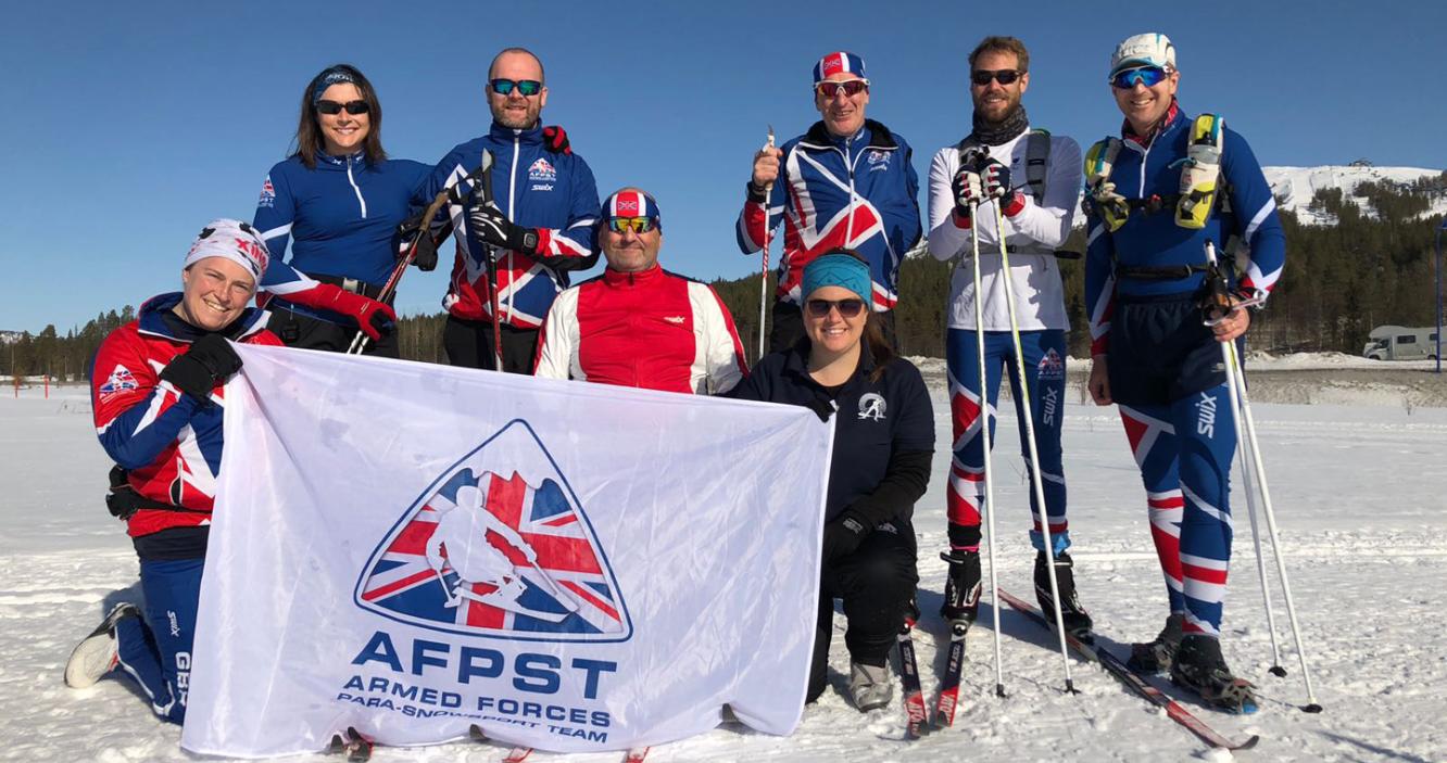 Group of Armed Forces Para Snow Team male and female skiers holding the charity flag in a snow landscape