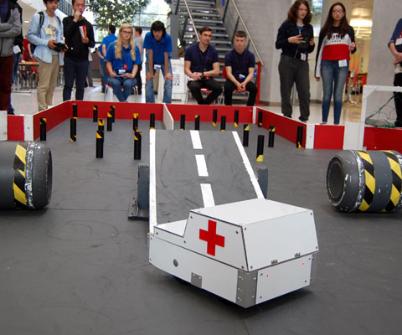 A Rampaging Chariots robot takes part in an obstacle course in the foreground, while a crowd of students watch on in the background