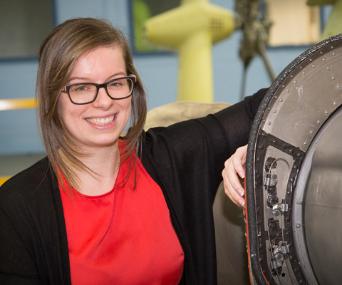 Young white female Leonardo engineer leans on large piece of machinery