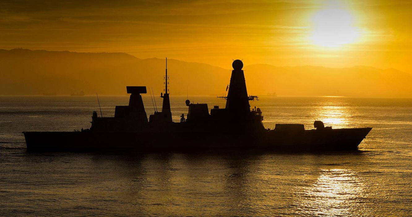 Frigate at sea silhouetted against an orange sunset
