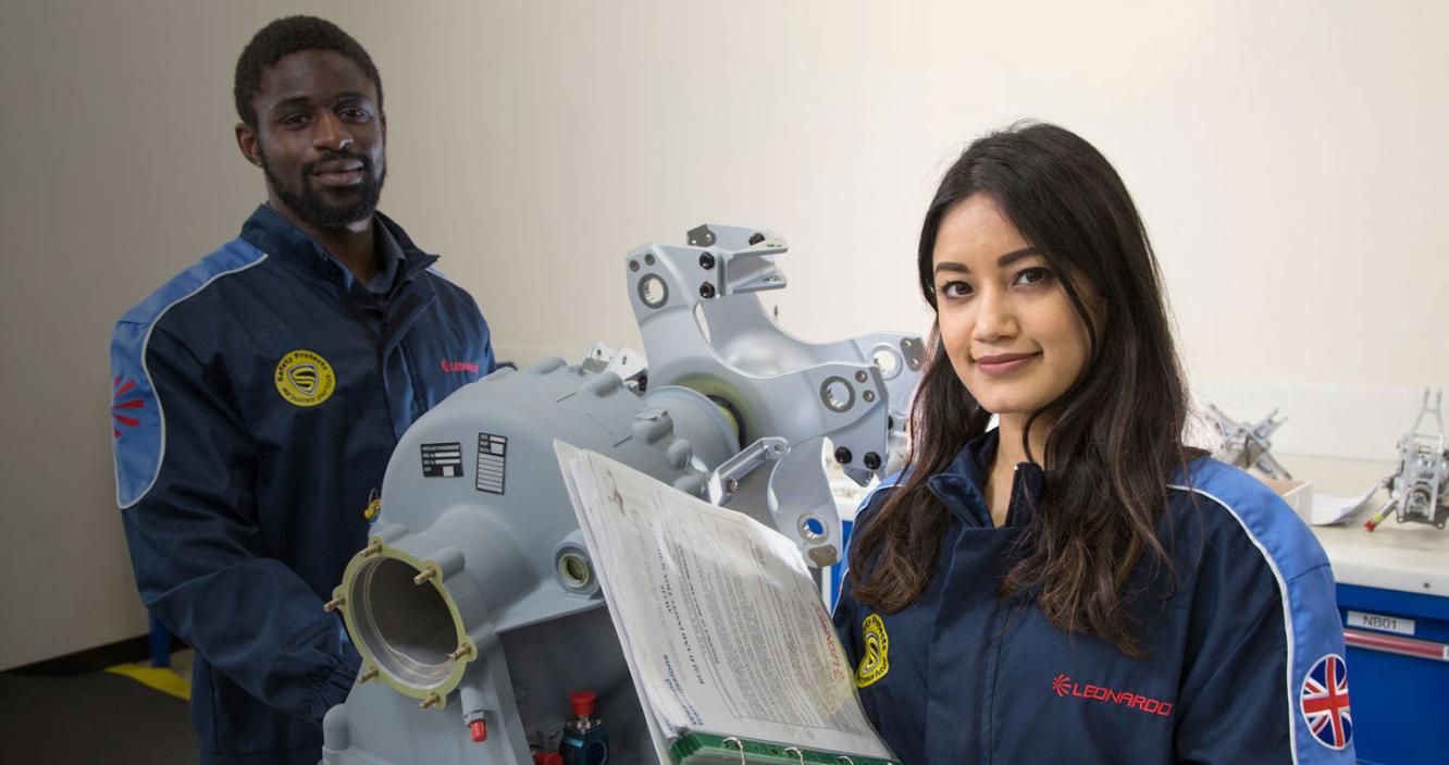 Young male and female engineer of different ethnicities smile and stand by machinery
