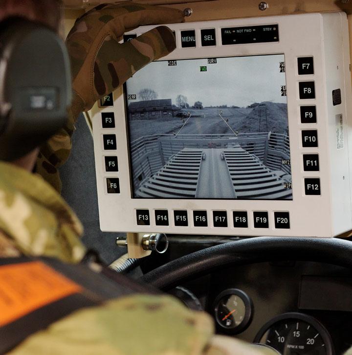 Man in camouflage holds ruggedised display showing thermal image on dashboard of vehicle 