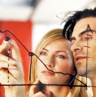 man and women looking at graph on a see-through graphics board